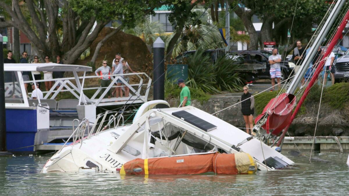 People look at a damaged boat in a marina at Tutukaka, New Zealand on Sunday after waves from a volcano eruption swept into the marina. — AP