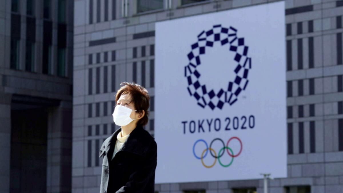 A woman wearing a protective mask walks near a banner of the Tokyo 2020 Olympics in Tokyo. — AP