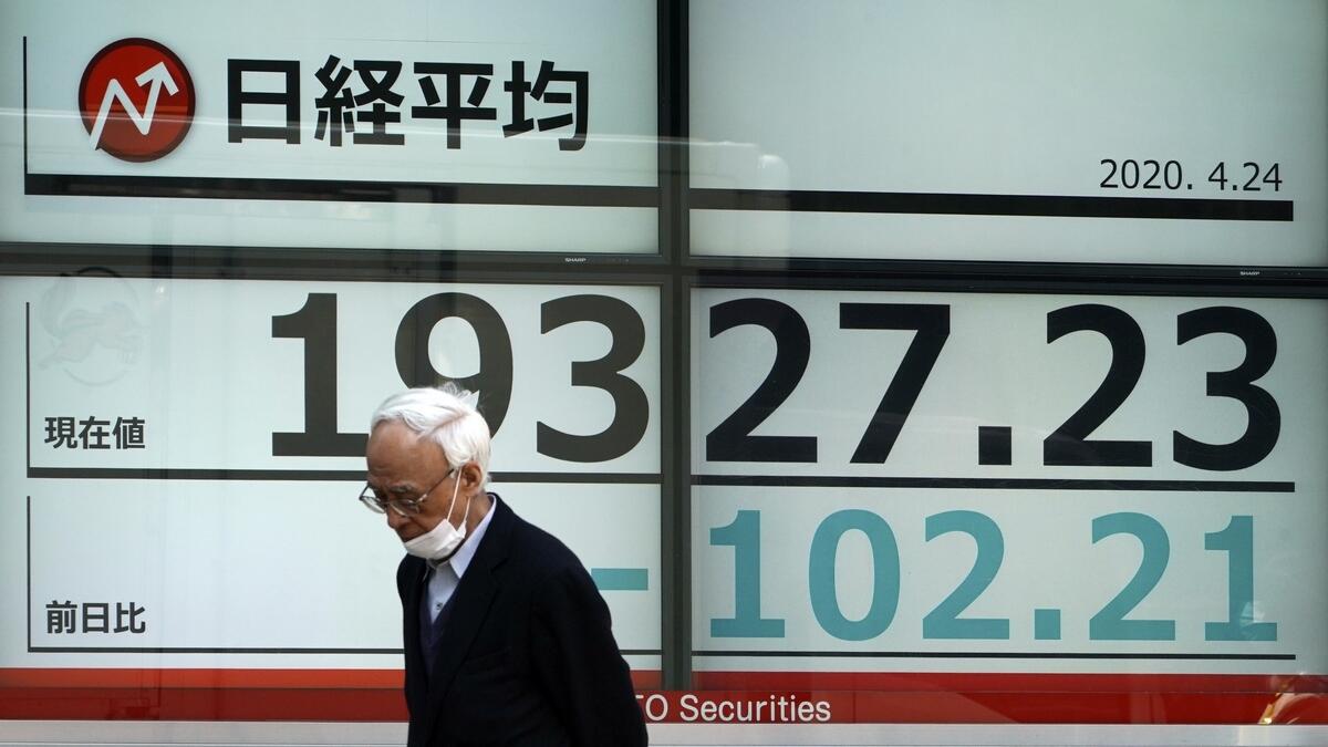 A man wearing a mask to help stop the spread of the new coronavirus walks past an electronic stock board showing Japan's Nikkei 225 index at a securities firm in Tokyo. - AP