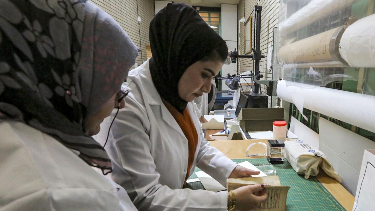 A conservator opens a manuscript undergoing restoration at the Iraqi Manuscript House's resoration lab in Iraq's capital Baghdad on December 6, 2022. — AFP