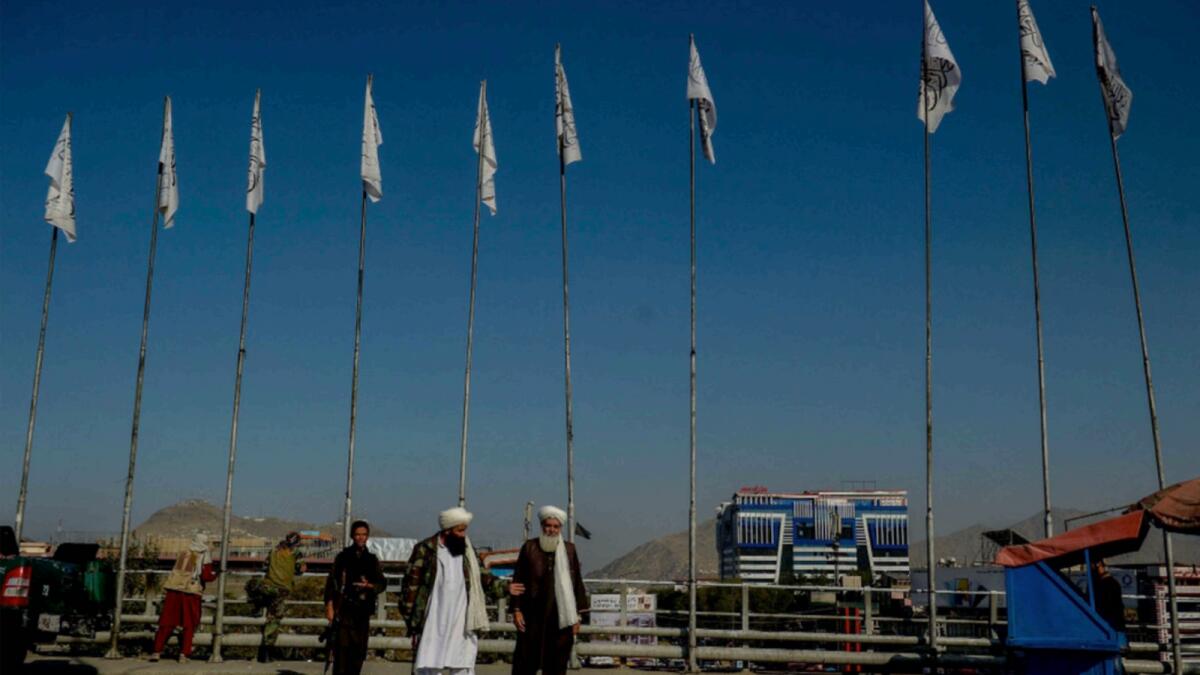 Taliban fighters walk as Taliban flags fly on poles along a street in Kabul. — AFP