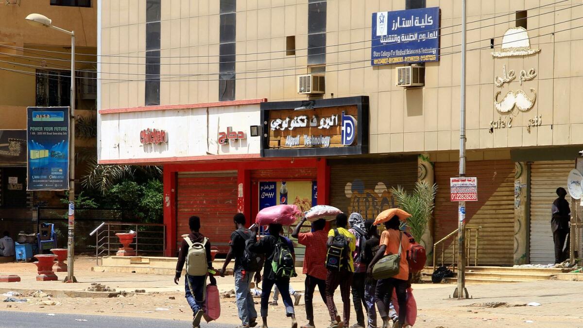 People carrying their belongings walk along a street in Khartoum on Sunday as fighting between the forces of 2 rival generals continues. — AFP